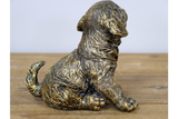 Bronze statue of a puppy on a wooden surface with a light gray background