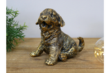 Bronze statue of a dog on a wooden surface with a plant and light bulb in the background