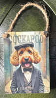 Decorative small metal sign with a Cockapoo dog wearing a hat and suit with a jute string to hang it.