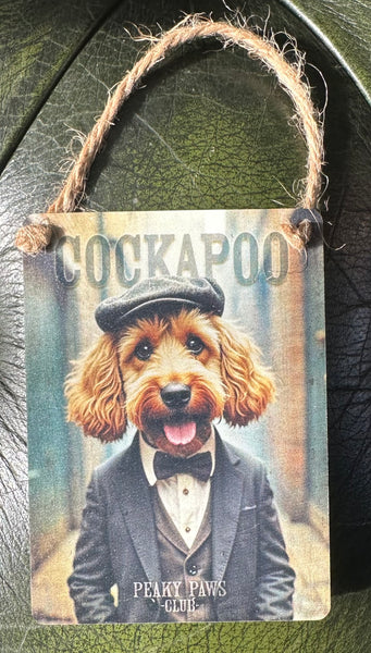 Decorative small metal sign with a Cockapoo dog wearing a hat and suit with a jute string to hang it.